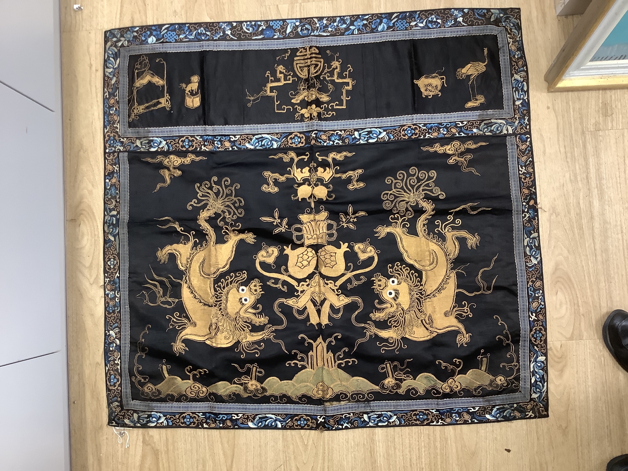 A 19th century Chinese dark blue ground panel, gilt thread embroidered with a pair of celestial dragons flying amongst precious objects, beneath a frieze, 95 x 95cm